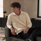 Off white cable knit half zip sweater worn seated indoors in a relaxed lifestyle pose.