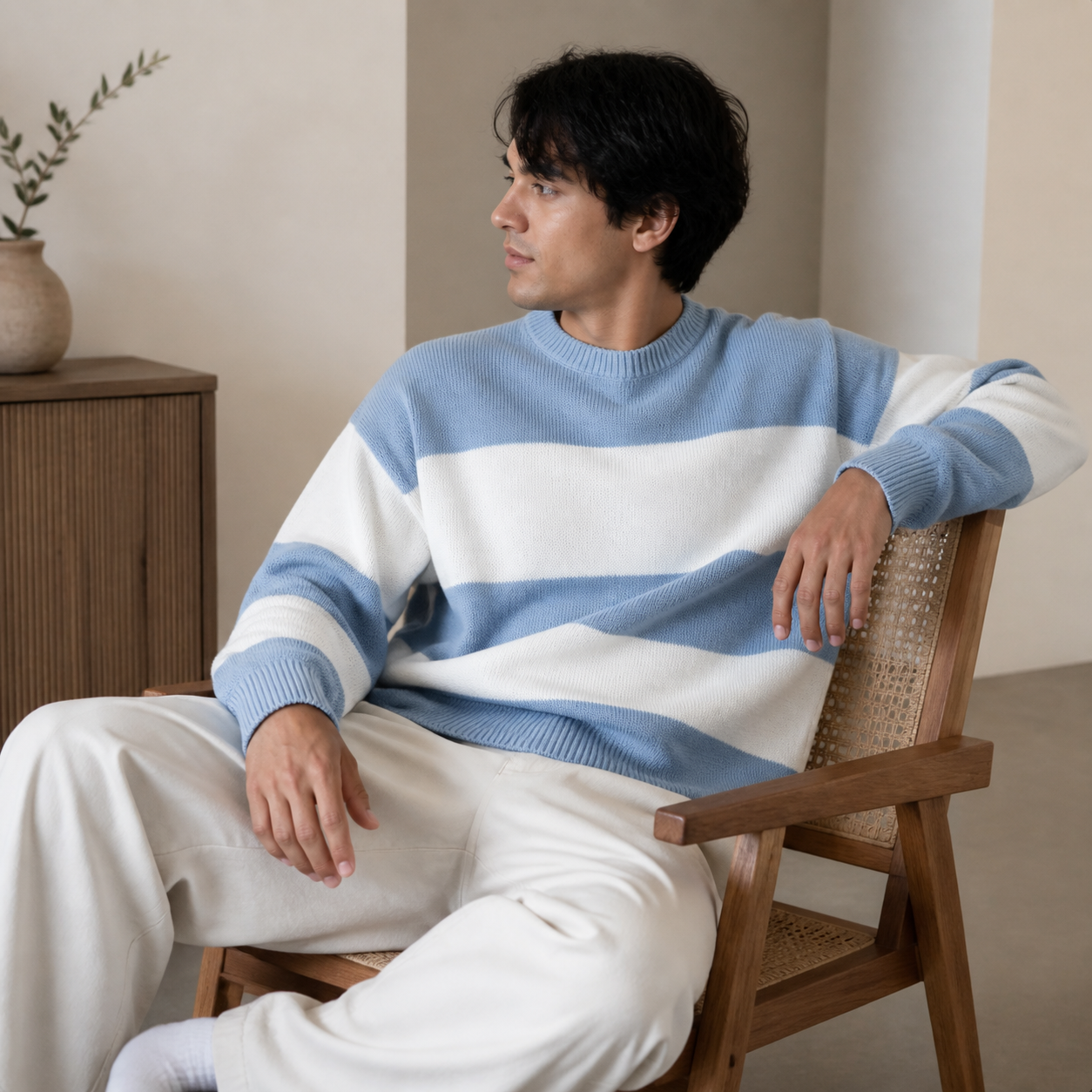 Light blue striped crew neck sweater worn seated indoors in a relaxed lifestyle pose.